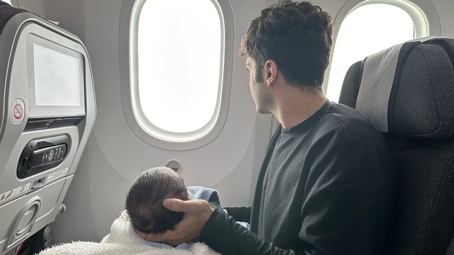 A father holding his newborn on the flight home, looking out of the aircraft window.